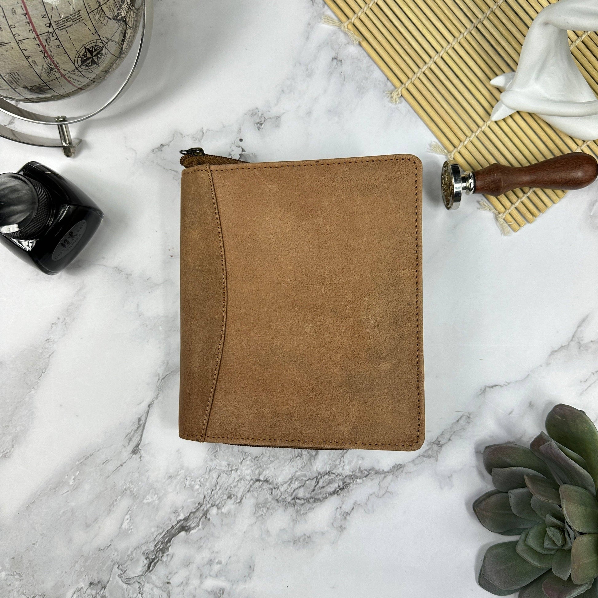 Brown leather 12 pen case on a marble surface with a globe, inkwell, and plant.