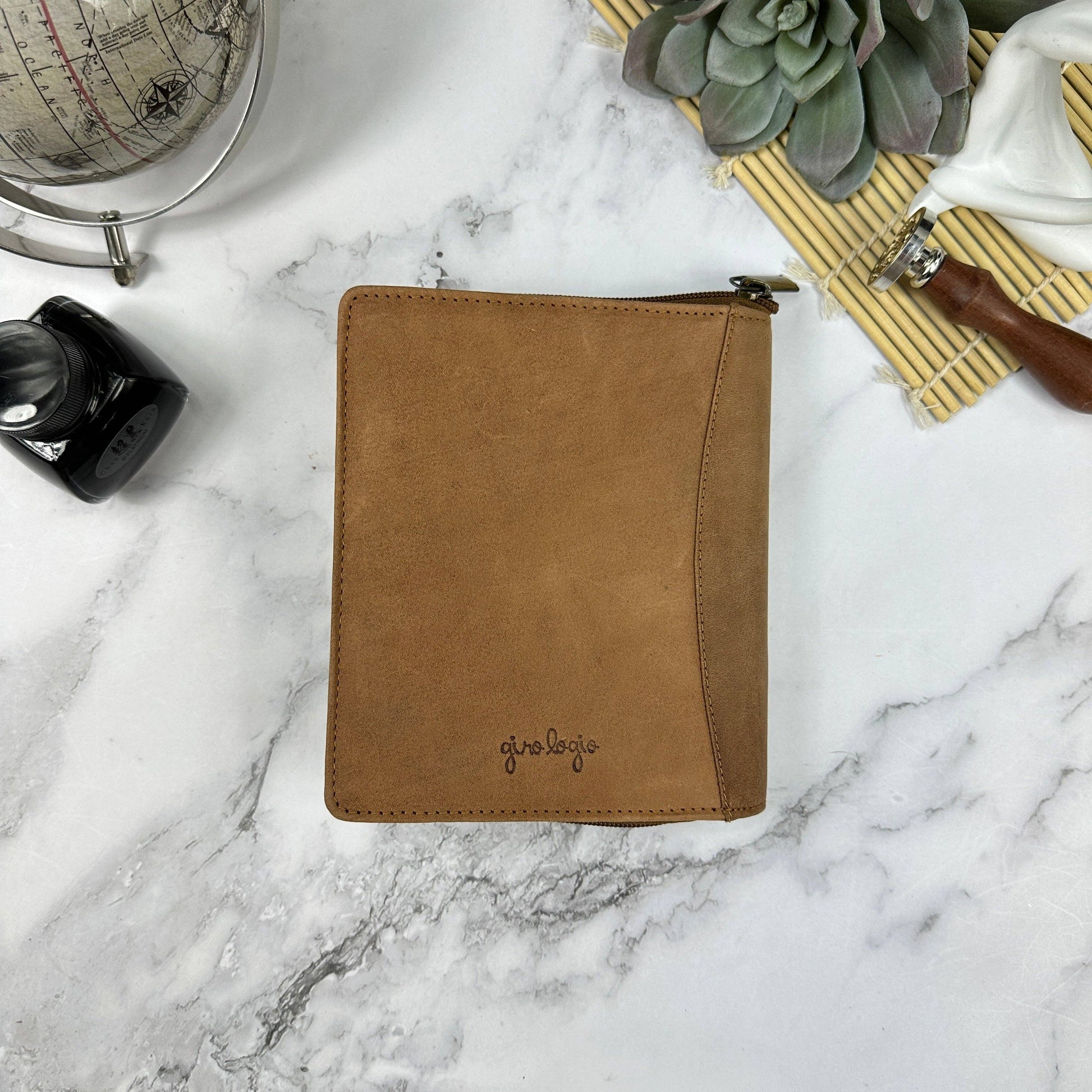 Brown leather pen case on a marble surface with decorative items.