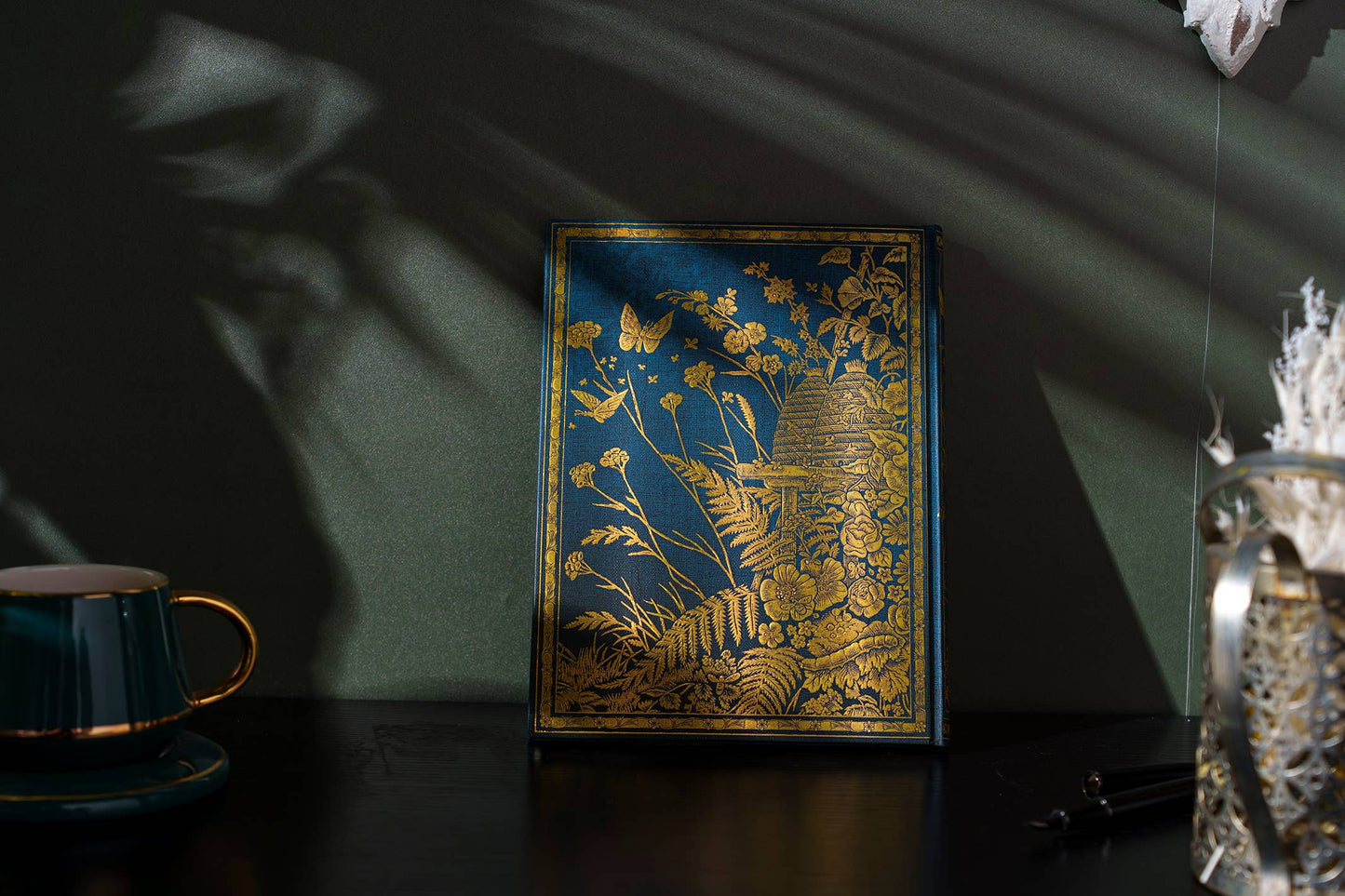 Decorative book with gold illustrations on a dark surface with a green wall background