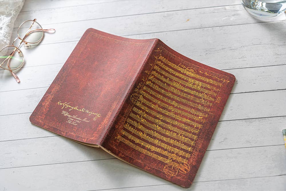 Open vintage book with gold text on a light wooden surface, accompanied by eyeglasses.