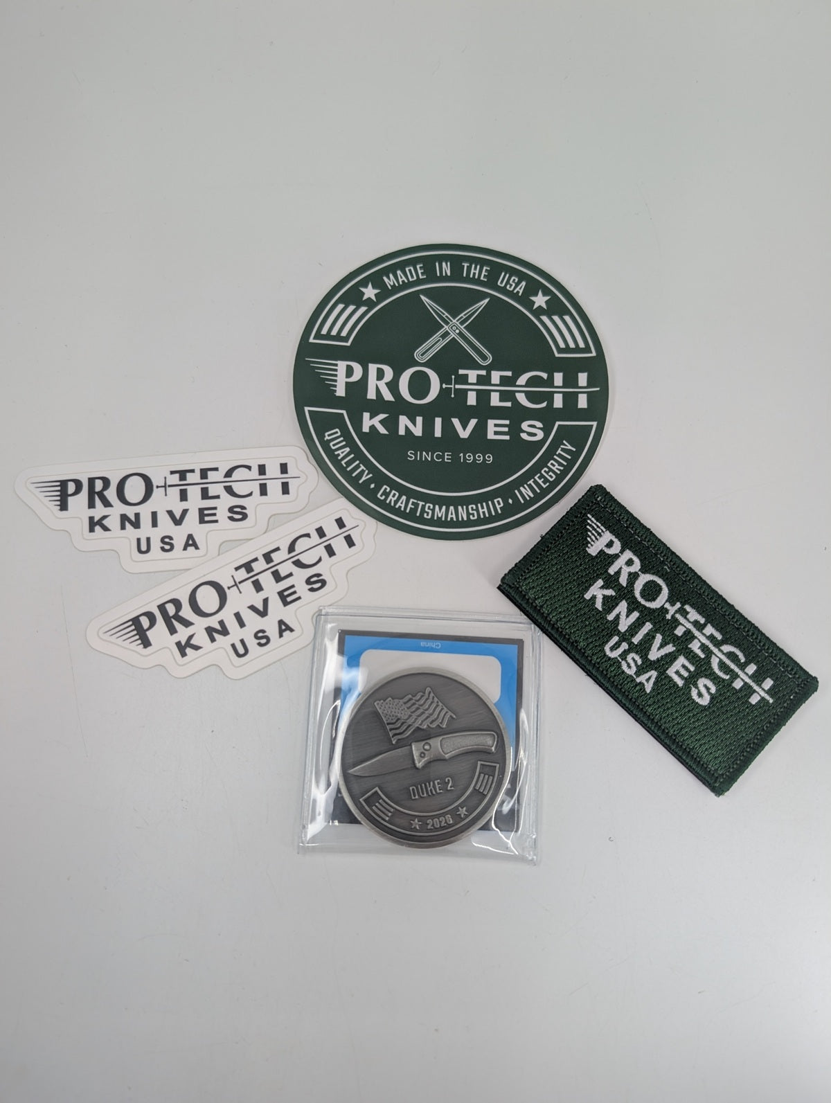 Pro-Tech Knives branding on various items, including a coin, patch, and stickers on a white background.