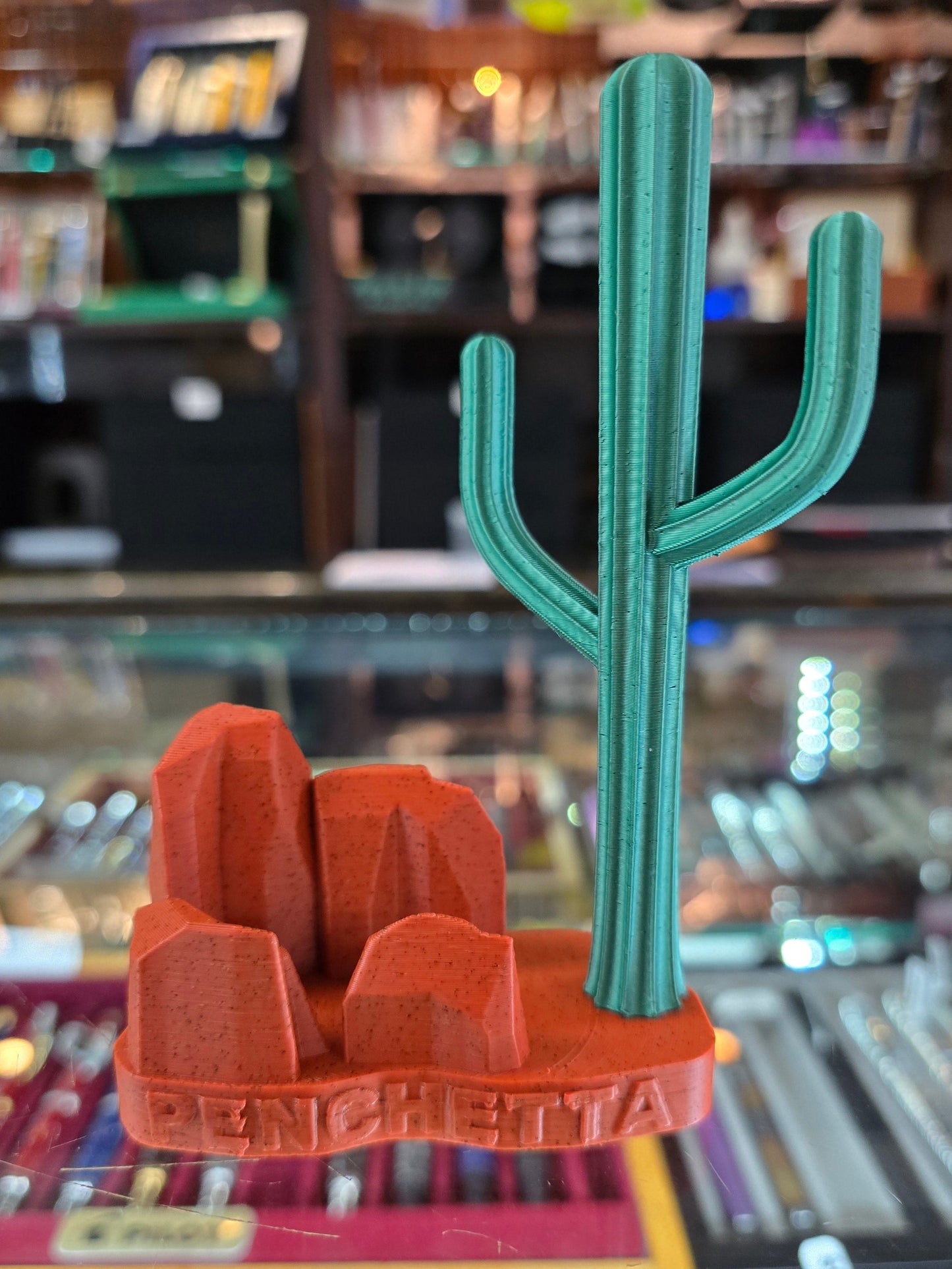 3D-printed green and red tool-like object on a reflective surface with a blurred indoor background