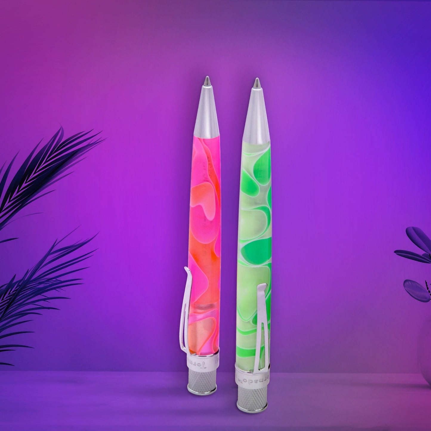 Two pen look like lava lamps standing upright on a surface against a purple and pink gradient background. One pen contains pink, orange, and yellow marbled look , and the other contains green and white marbled acrylic.