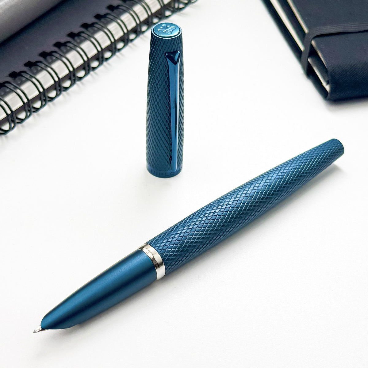 Blue Diplomat Viper pen with textured design on a white surface, next to a spiral notebook.