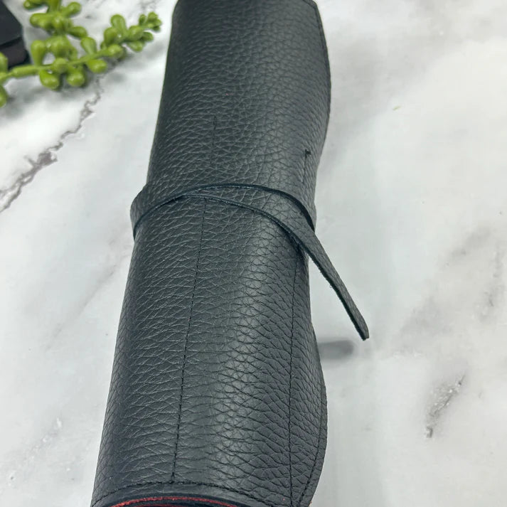 Black textured pen roll on a marble surface with greenery.