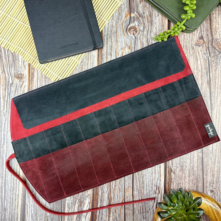 Black and red clutch pen roll on a wooden surface with a plant and notebook.