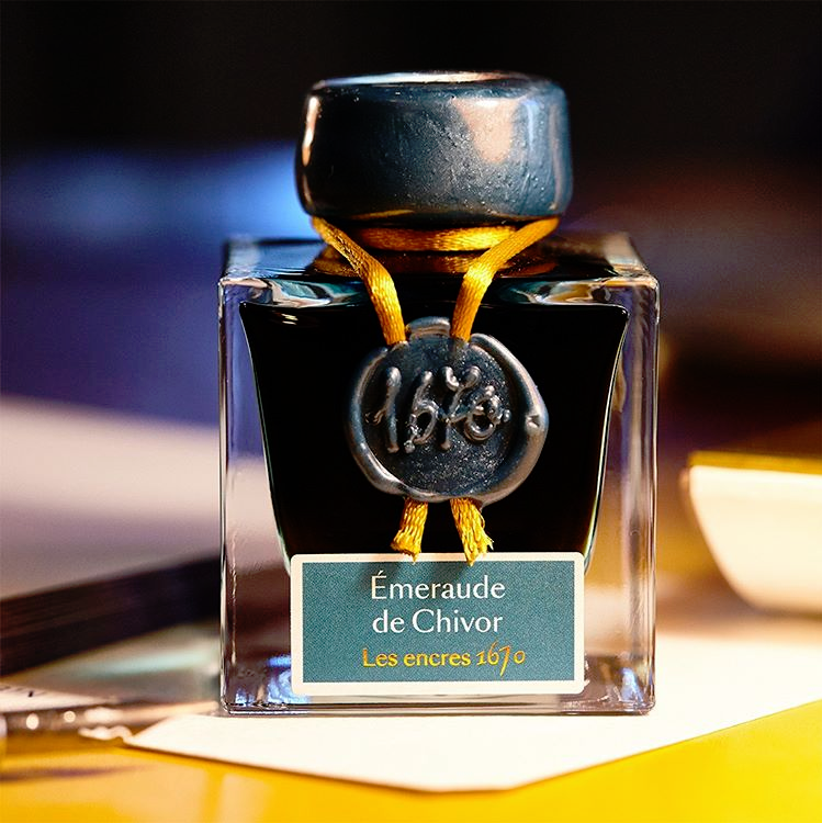 Ink bottle labeled 'Emeraude de Chivor' with decorative elements on a blurred background