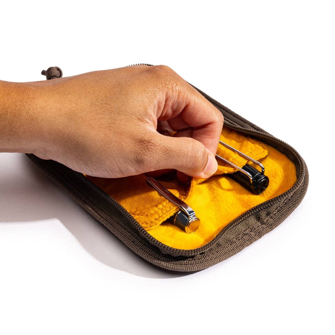 Hand opening a LOCHBY Duo pen case with yellow interior on a white background