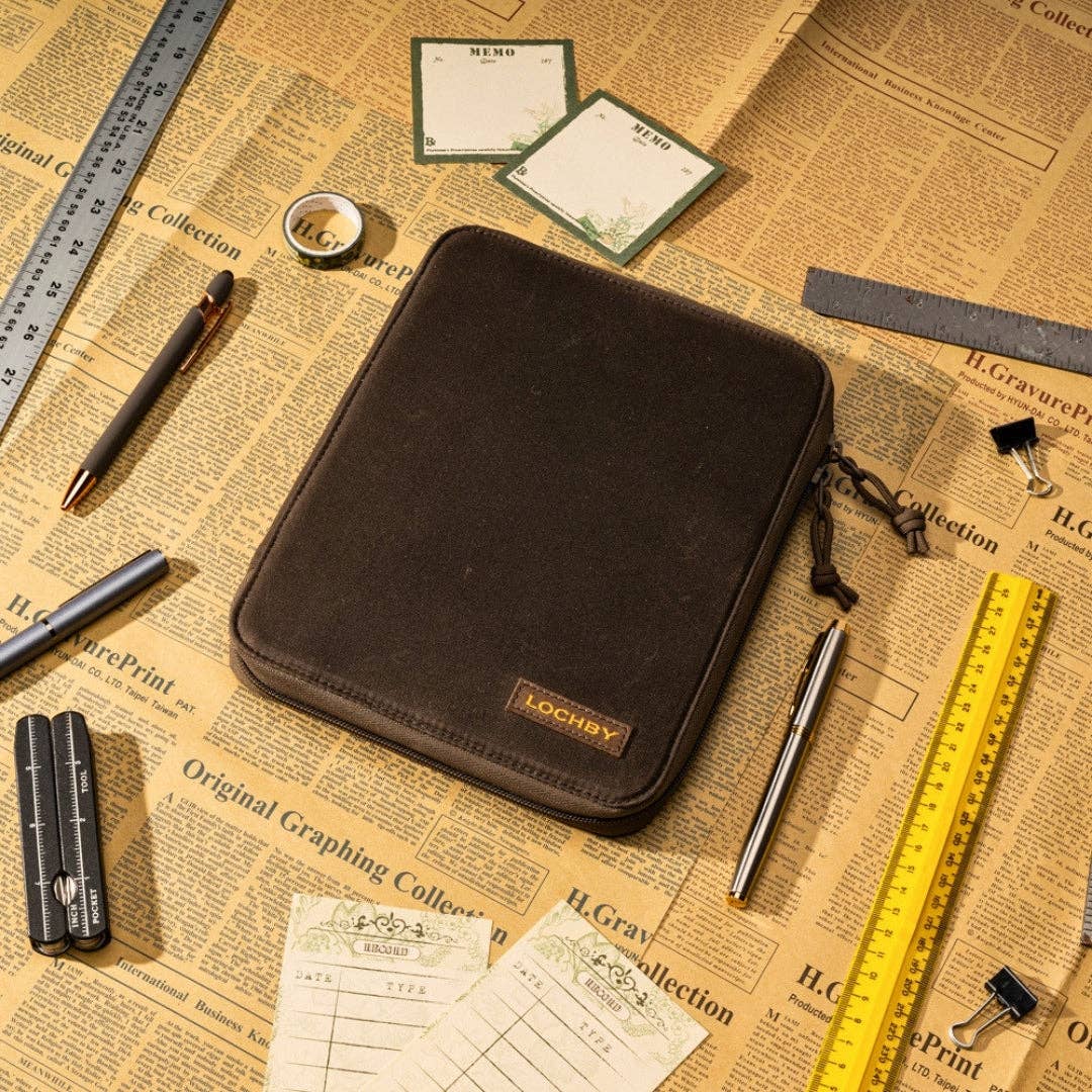 Brown leather case with 'Lochby' branding on a vintage newspaper background with stationery items.