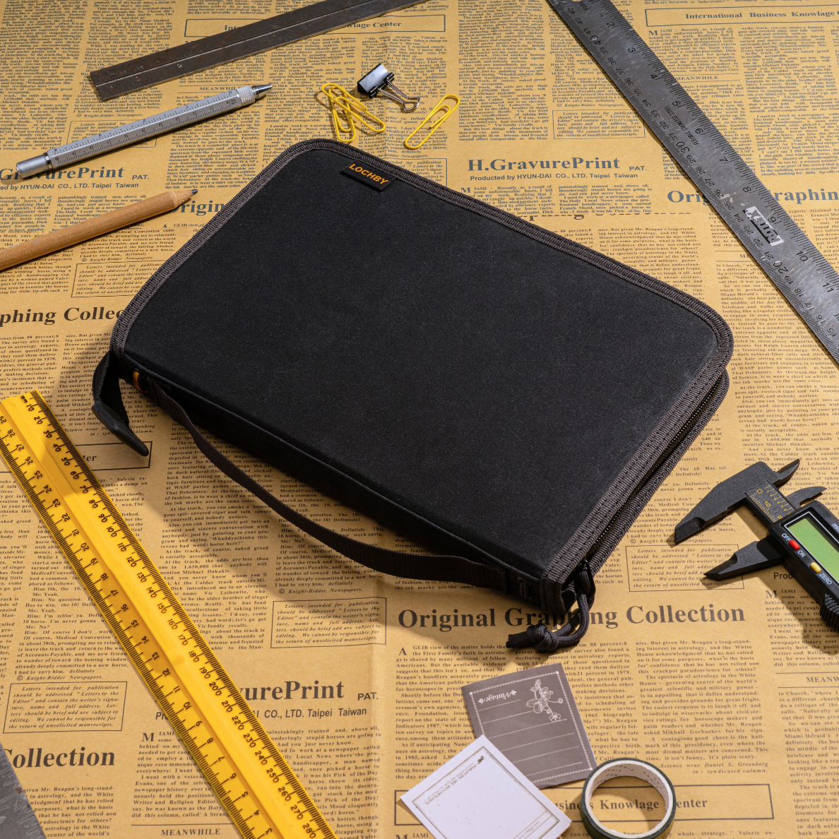 LOCHBY Field Folio A5 Black zippered on a newspaper background with tools and stationery items.