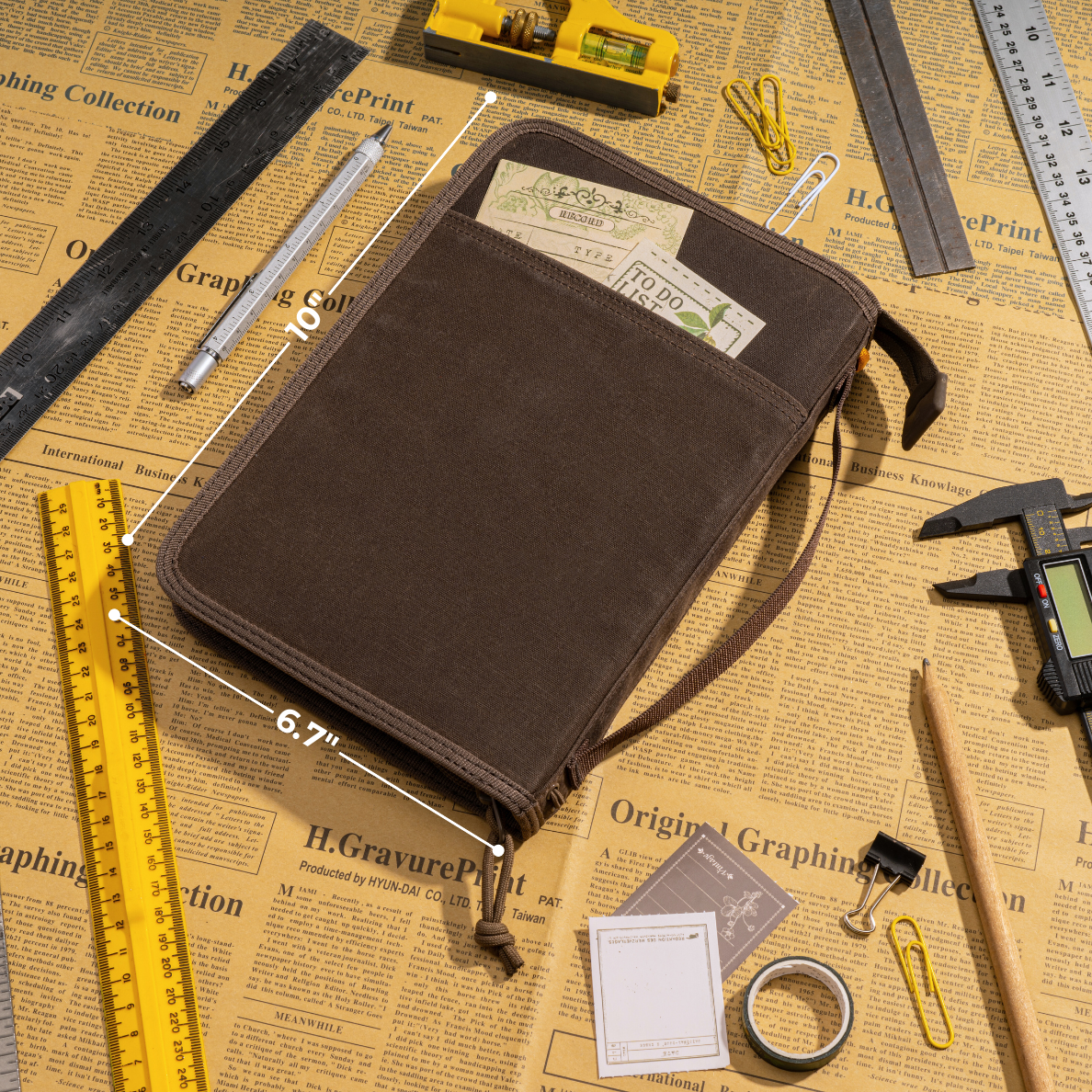 Brown LOCHBY Field Folio A5 pouch with compartments on a newspaper background with stationery items.