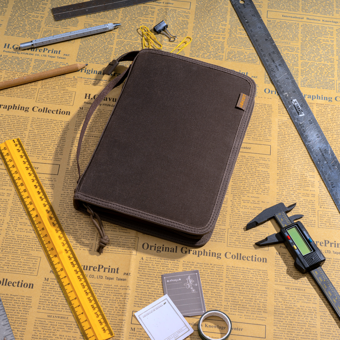 Brown canvas case on a newspaper background with measuring tools around