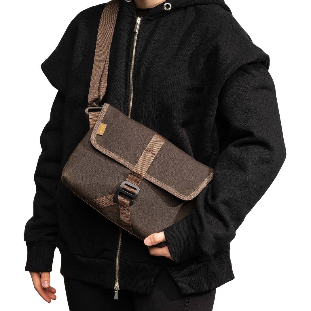 Person wearing a black hoodie holding a brown LOCHBY Field Sling bag on a white background
