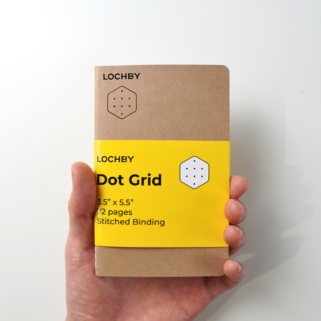Hand holding a Lochby notebook with a yellow label on a white background