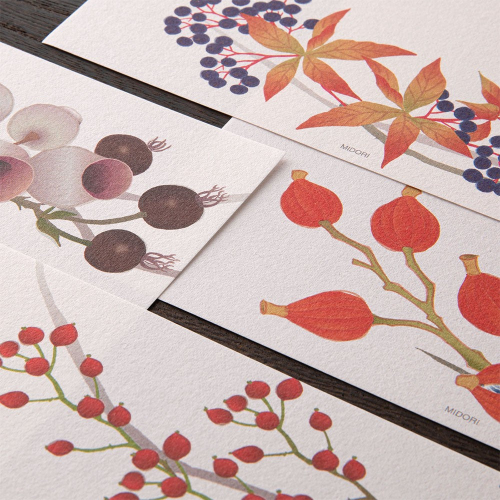 Set of stationery items with floral and berry designs on a wooden surface.