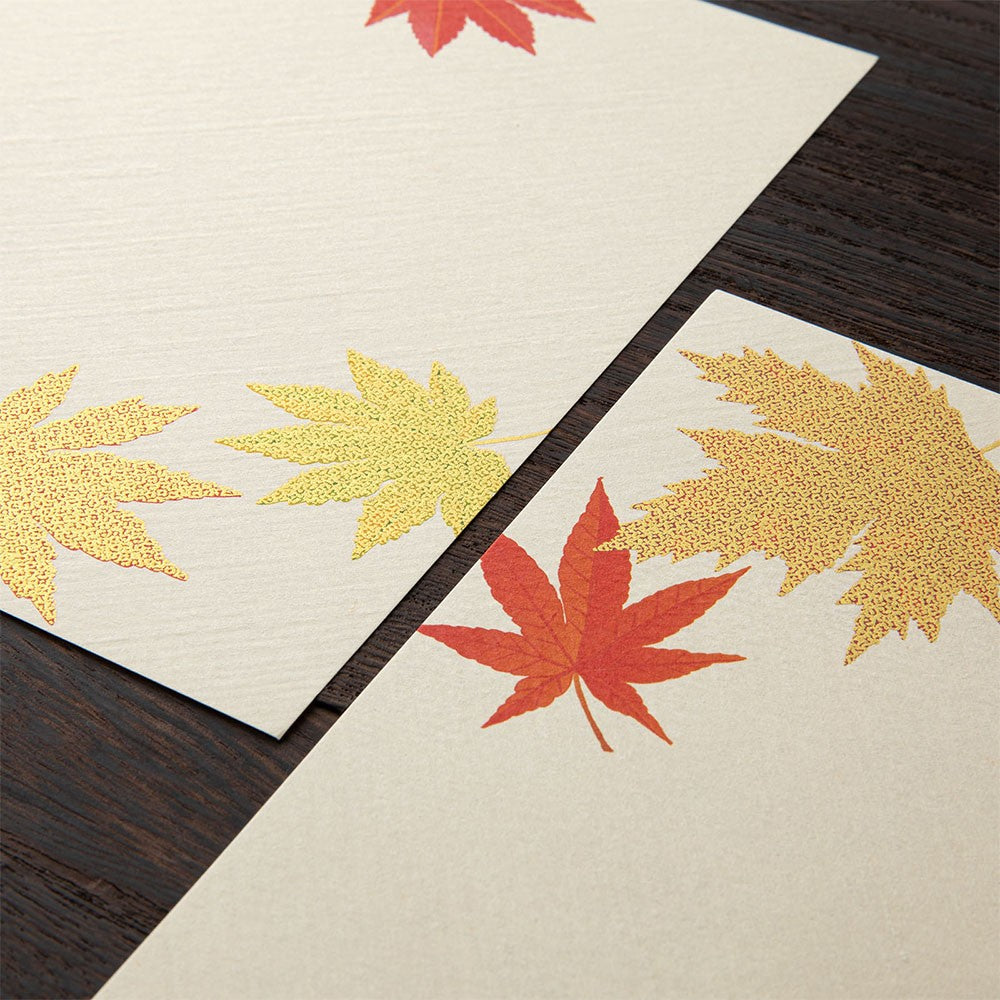 Two beige letter pads with red and gold leaf patterns on a dark wooden surface.
