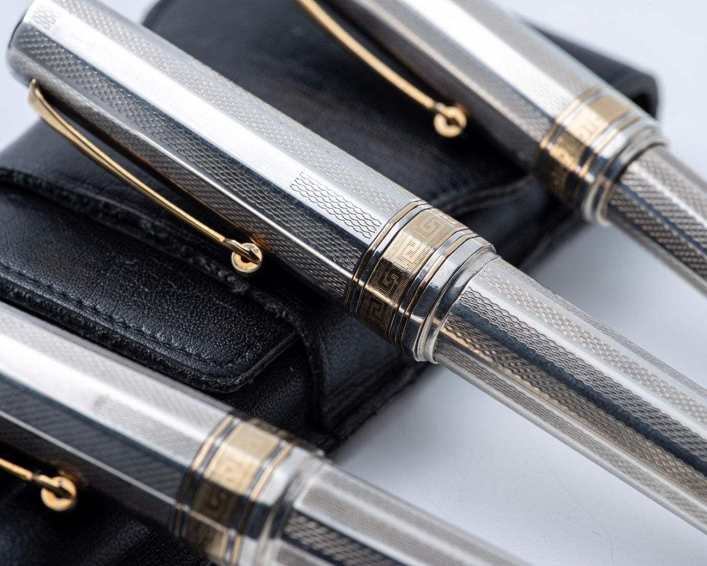 Close-up of a silver and gold pen with textured finish on a black leather surface.