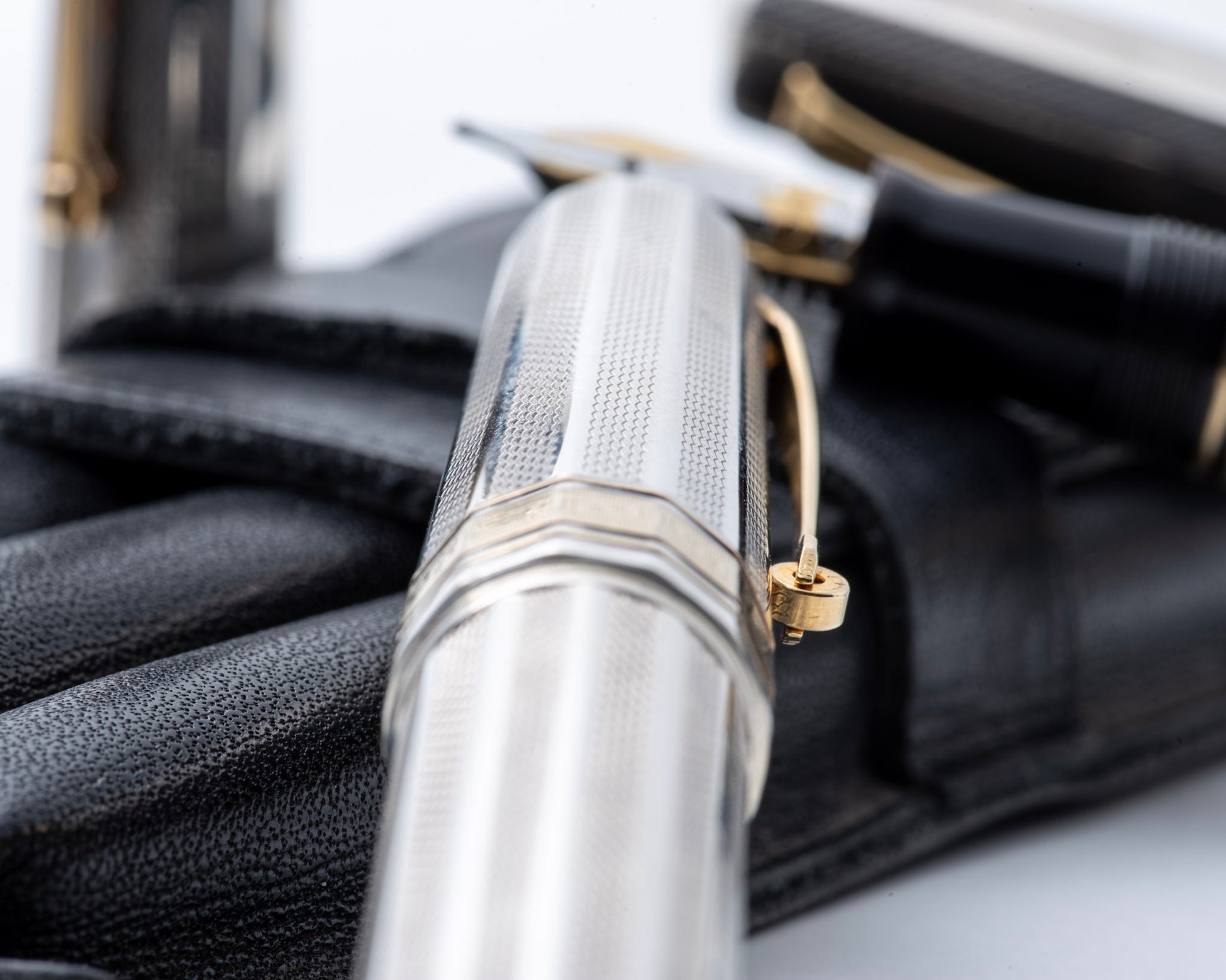 Close-up of a silver pen with a gold clip on a black leather surface.