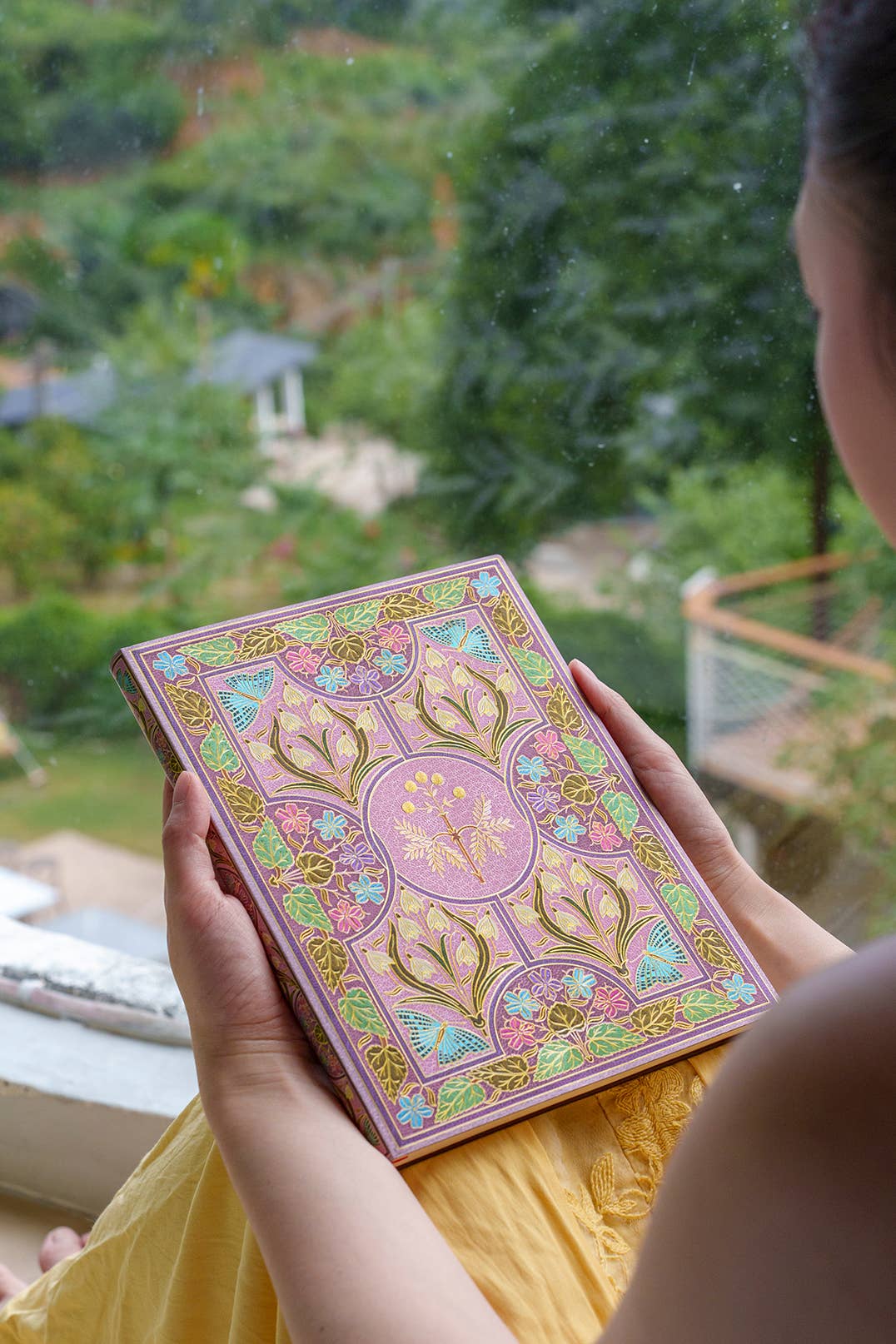 Person holding a decorative book with a garden view in the background