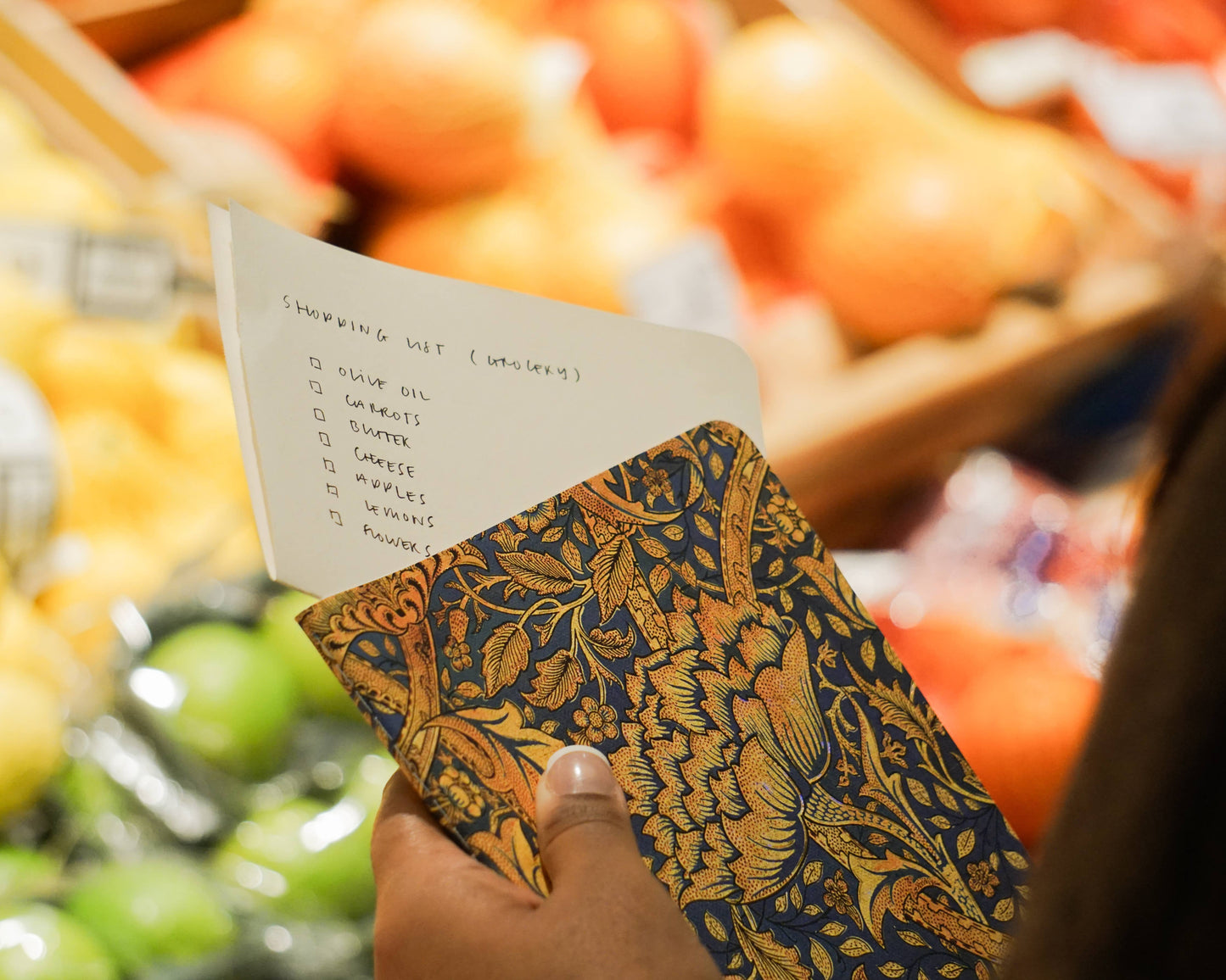 Hand holding a patterned notebook with a shopping list in a grocery store setting