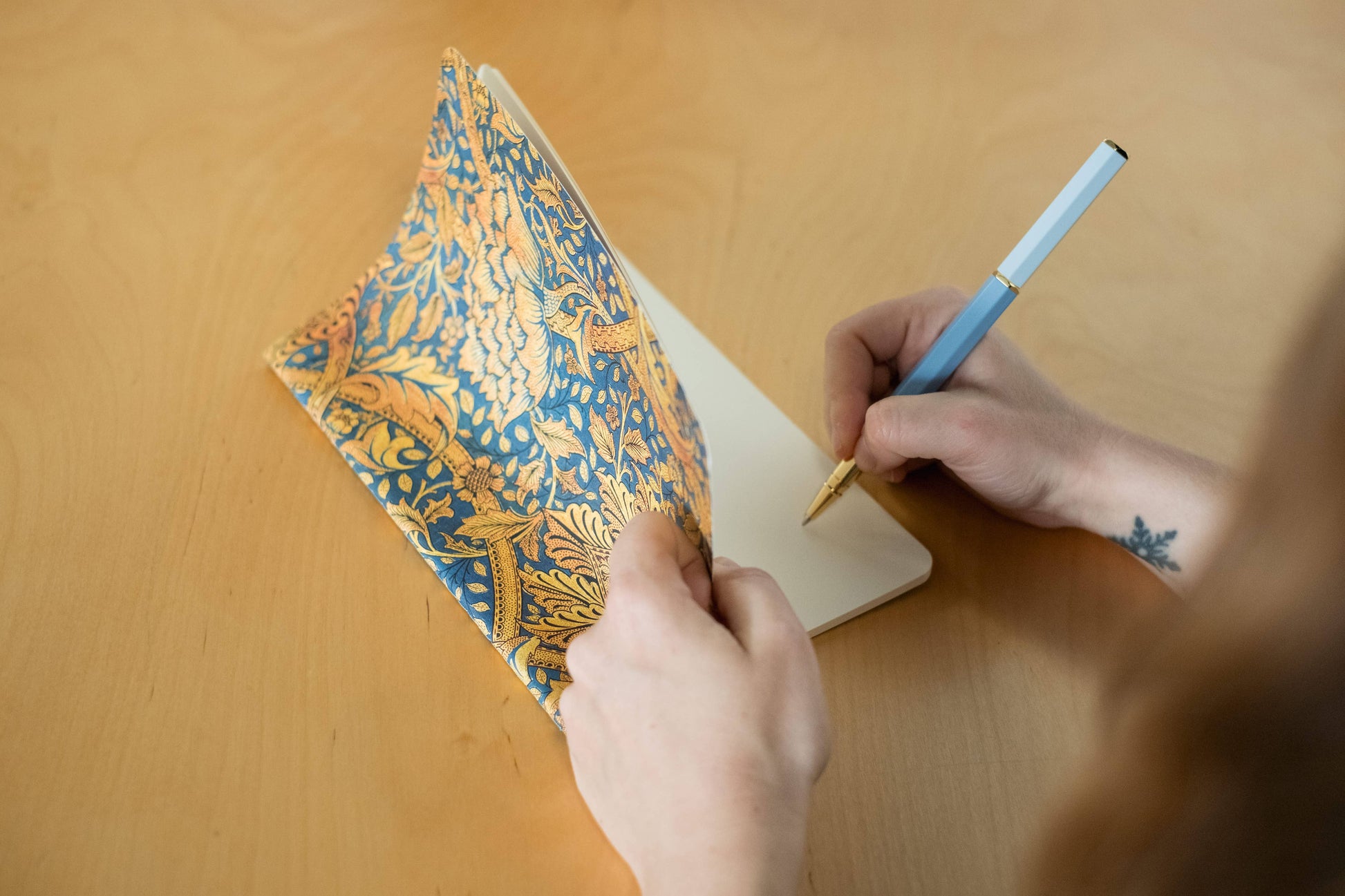Person writing in a notebook with a decorative cover 