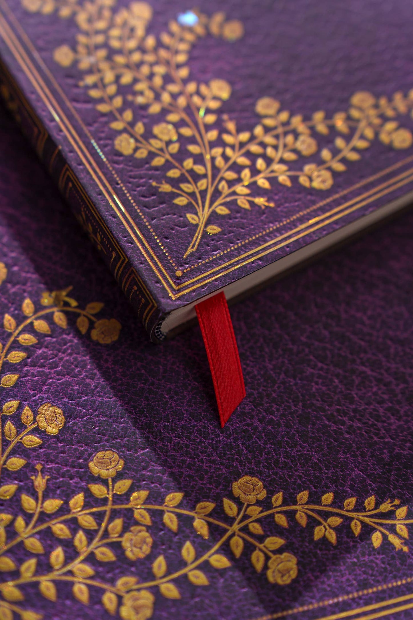 Purple book with gold floral patterns and a red bookmark on a matching purple background