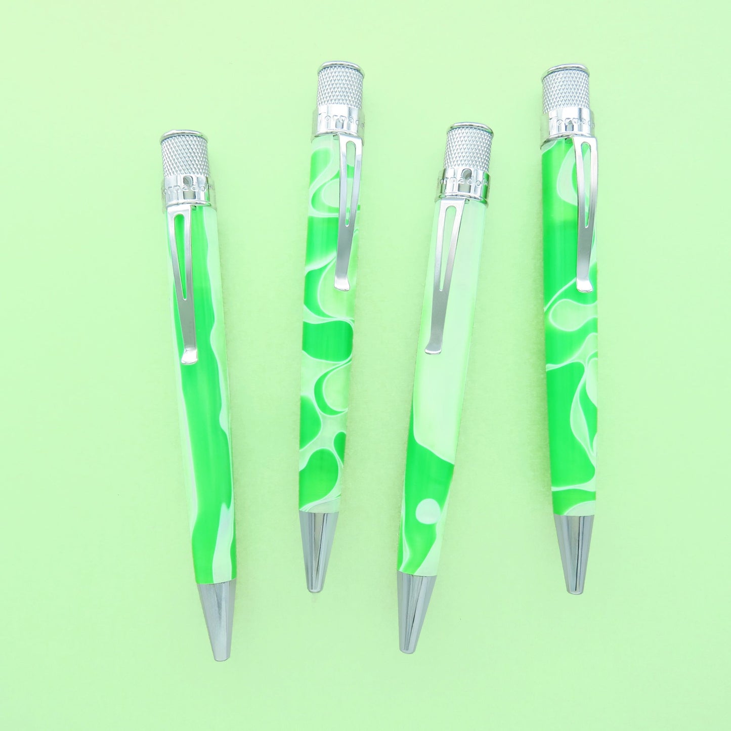 Four ballpoint pens with green and white marbled handles and silver metal accents, arranged vertically on a light green background.