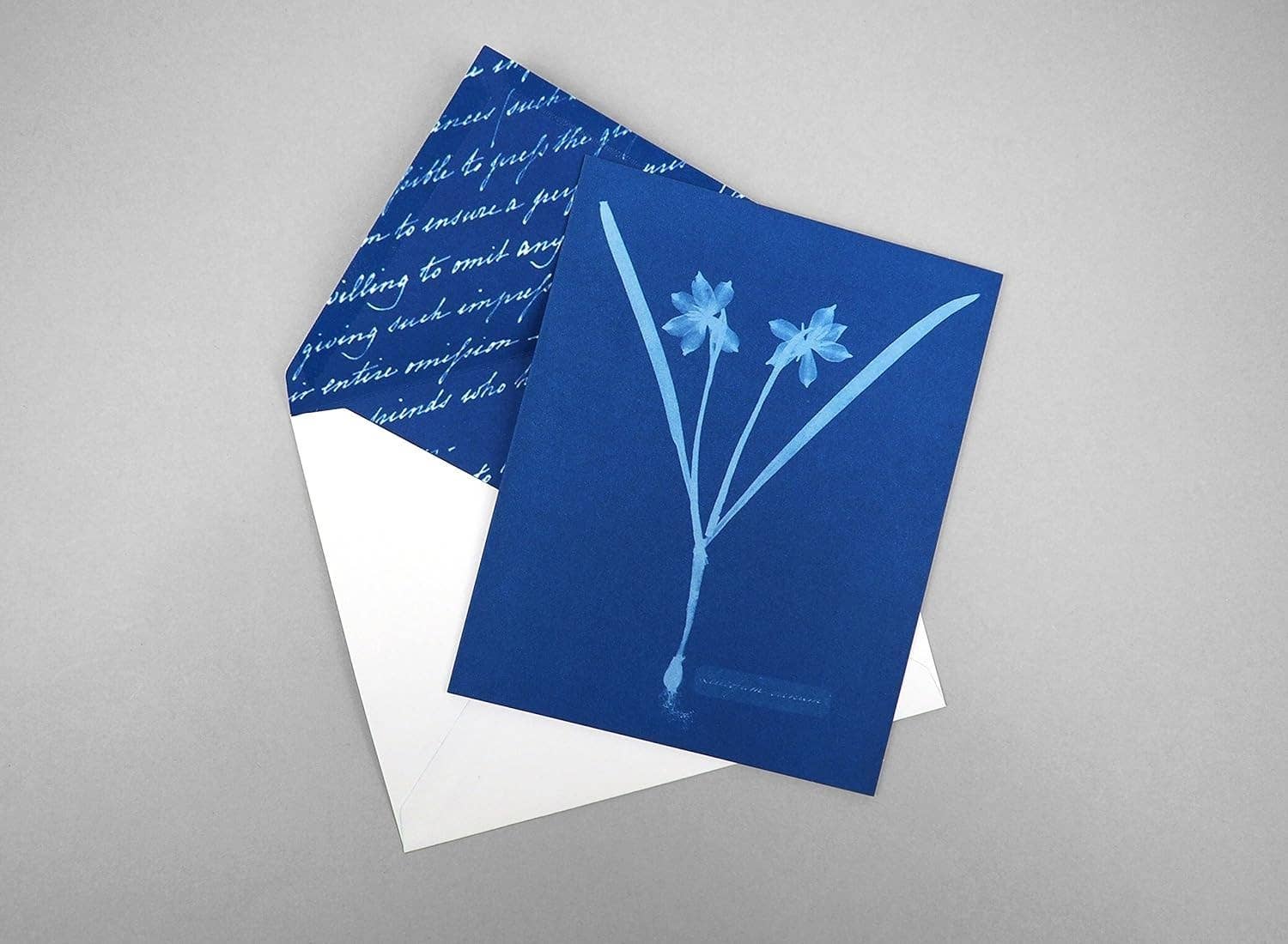 Blue greeting card with floral design and white envelope on gray background